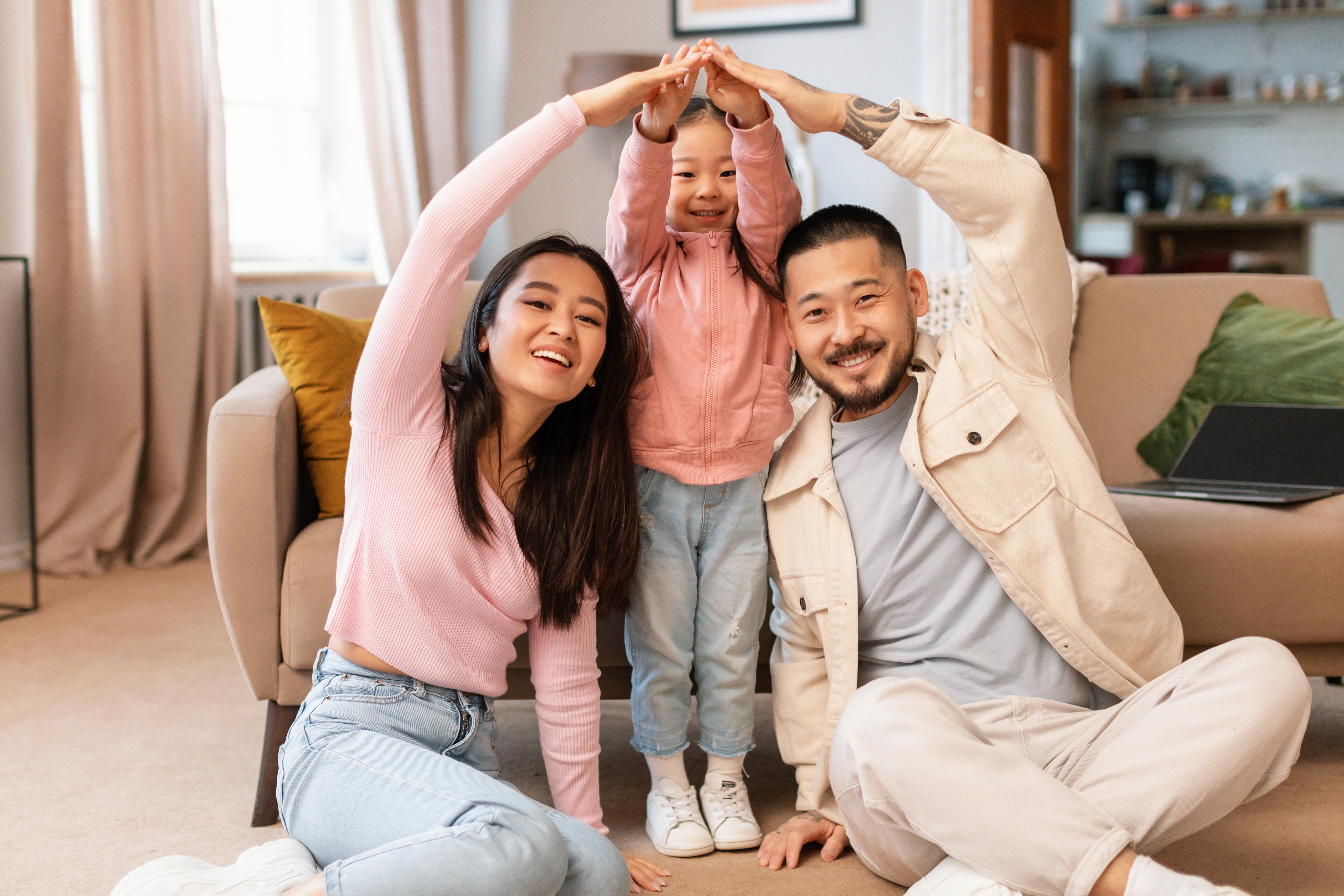 Asian Family With Child Celebrating Homeownership Doing Roof Gesture Indoors